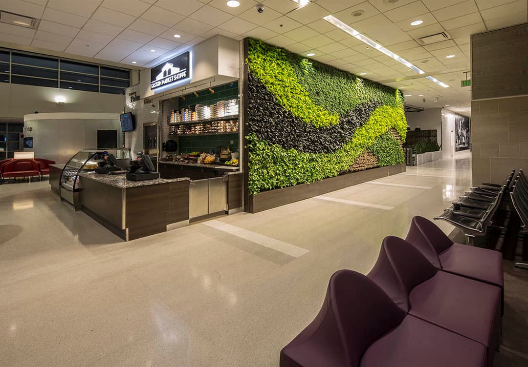 Airport terminal interior featuring a café with a green living wall and modern seating area.