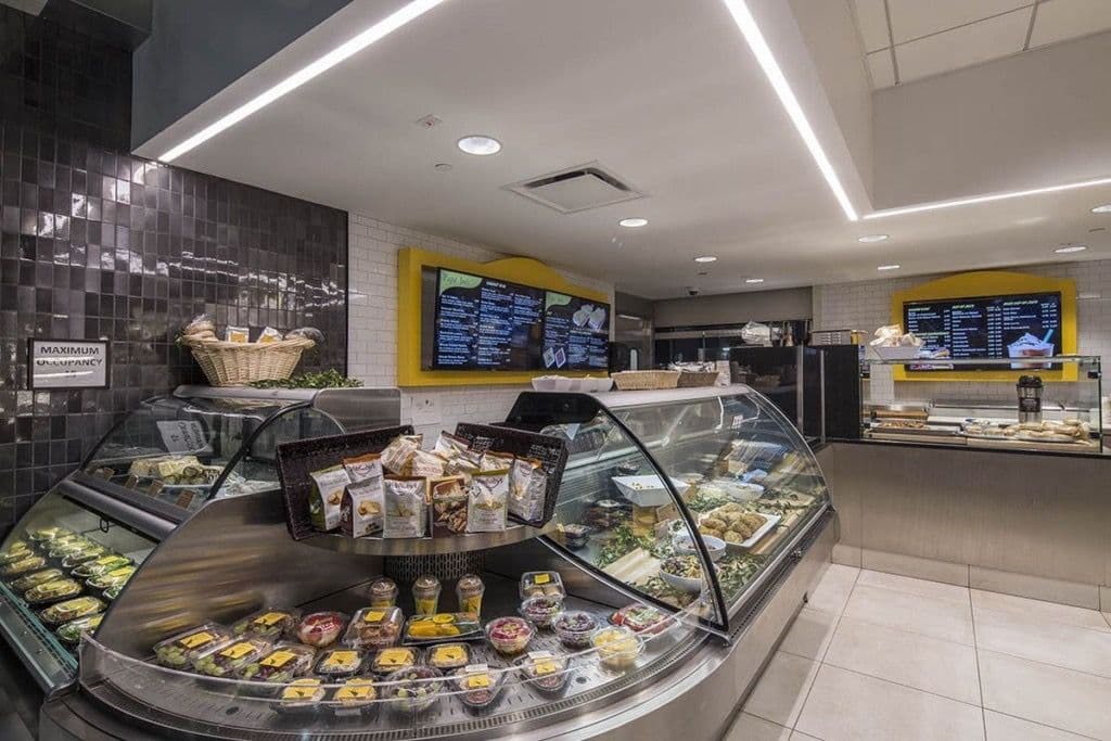 Modern deli display showcasing a variety of pastries and meals with digital menus above.