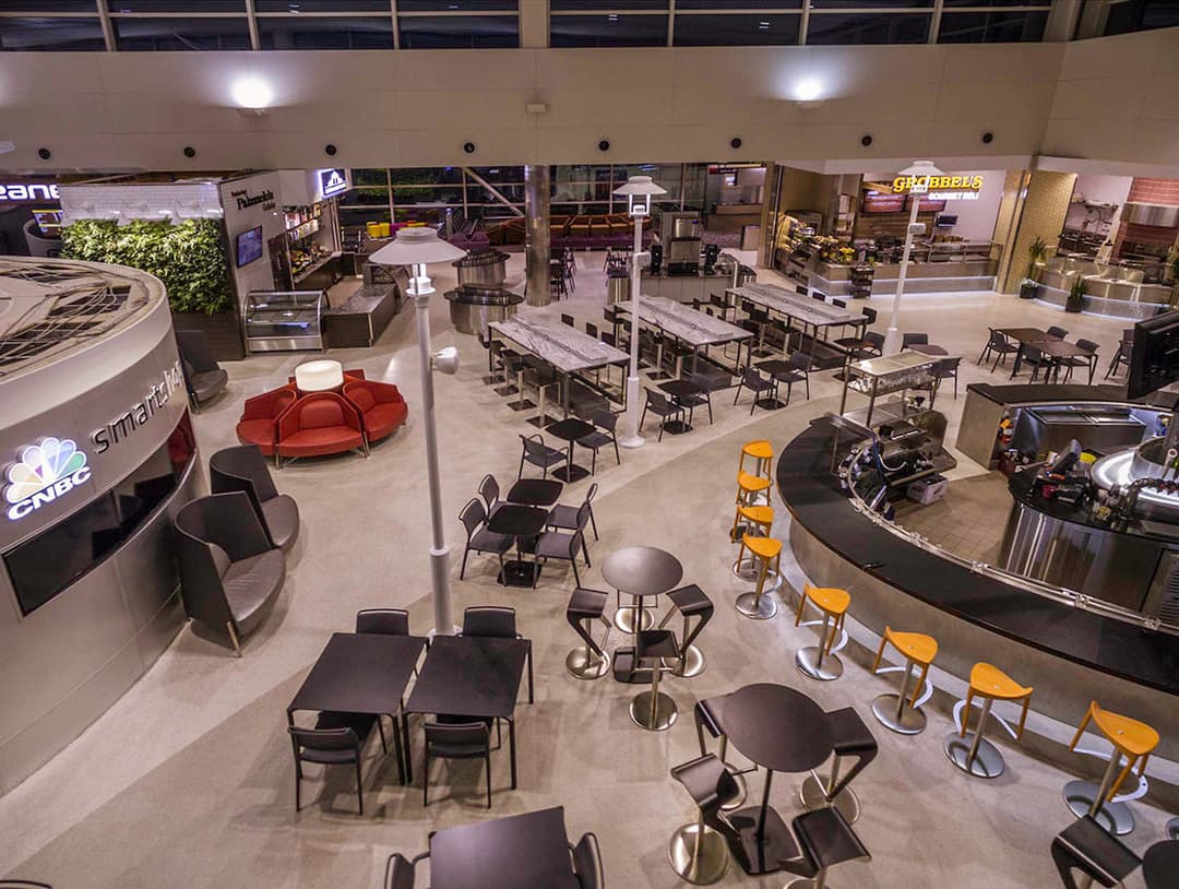 Modern airport dining area with tables, chairs, and various food options.