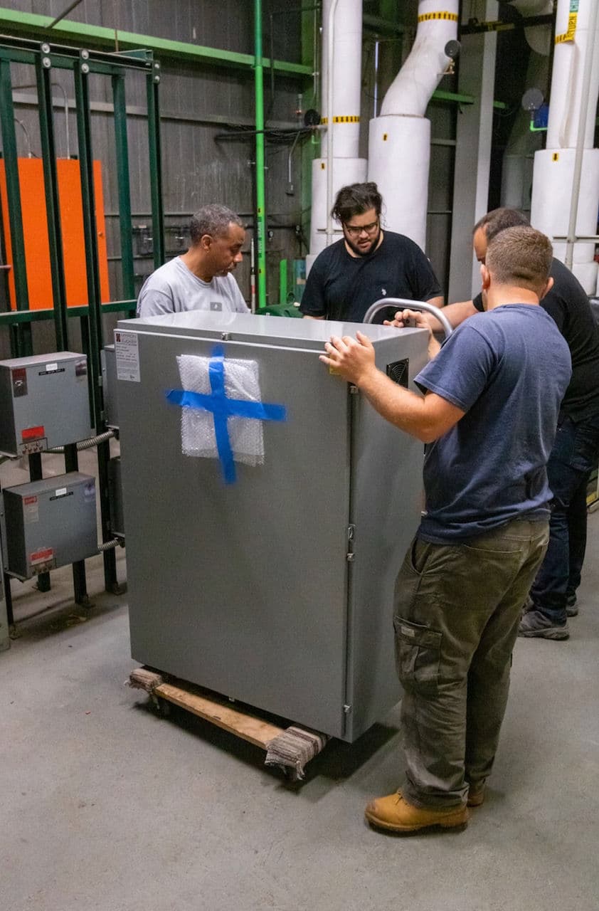 Five men carefully moving a large metal cabinet in an industrial setting.