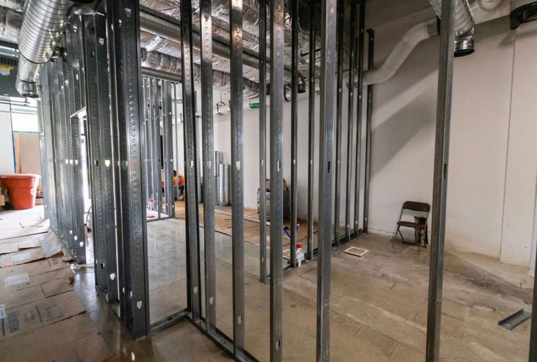 Interior construction site with steel framing and unfinished walls, featuring a chair and tools.