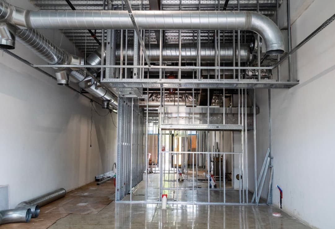 Interior view of a construction space with metal framing, ducts, and unfinished flooring.