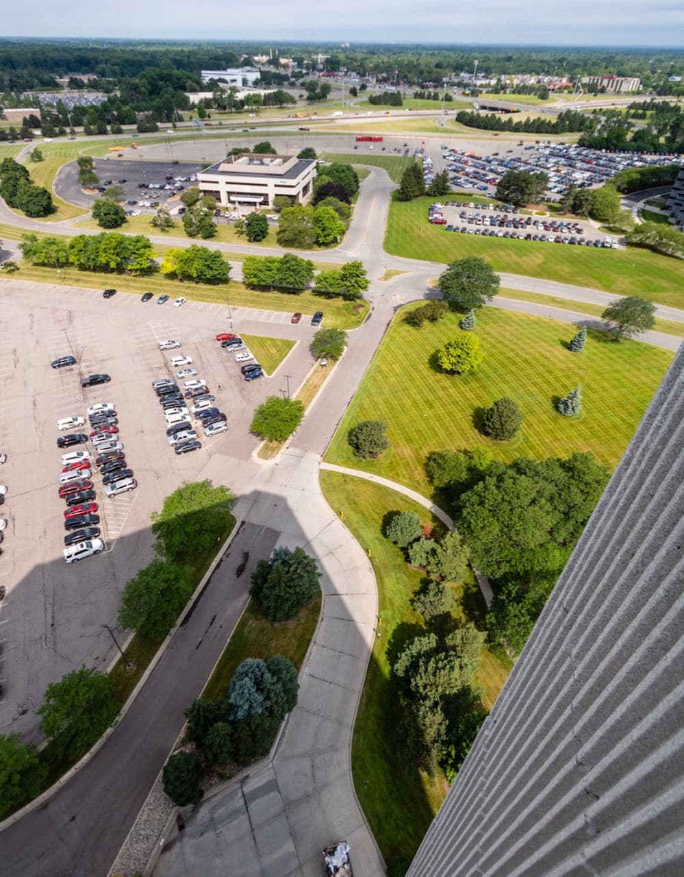 Aerial view of a parking lot, winding road, and green landscape near a commercial area.